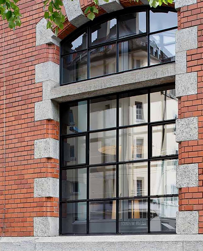 Grande fenêtre cintrée en acier noir dans une façade en brique